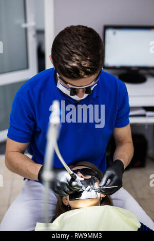 Mann an Zahnarzt Klinik erhält der zahnmedizinischen Behandlung ein Loch in einen Zahn zu füllen. Zahnersatz und Verbundmaterial Polymerisation Behandlung der Zähne. Stockfoto