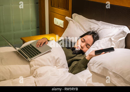 Junge asiatische Frau schlafend auf dem Bett nach Arbeiten am Laptop in der Geschäftsreise Stockfoto