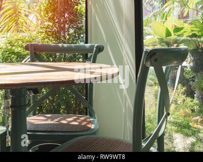 Close-up vintage Holztisch und grünen Stuhl in der Ecke des Restaurant mit Fenster Glas in der Nähe des Garten. Stockfoto