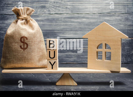 Eine Geld-Beutel und Holzklötze mit dem Wort kaufen und eine Miniatur Haus auf einer Waage. Die Anhäufung von Geld für den Kauf von Immobilien. Der Kauf einer Uhr Stockfoto