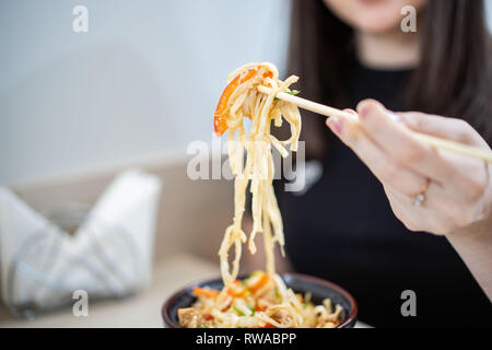 Nahaufnahme der menschlichen Hand packte Nudeln mit Stäbchen aus einer Schüssel mit heißer Nudelsuppe. Stockfoto