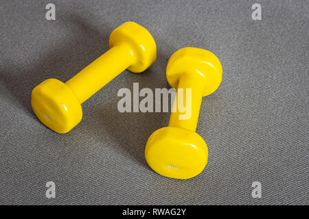 Gelbe Kurzhanteln auf grau Fitness Matte. Konzept der Fitness- und Gewichtsverlust. Stockfoto