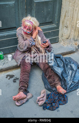 Rom - 18. Juni 2014: Eine obdachlose Frau trinkt Bier und setzt auf Make-up. Senior arme Frau sitzt auf dem Boden. Stockfoto