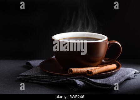 Dampfende Tasse Kaffee und Zimtstangen auf einem blau serviette vor einem schwarzen Hintergrund mit Kopie Raum Stockfoto