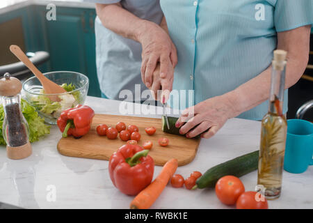 Senior paar Kochen einen Salat. Mann hilft Frau Gemüse zu schneiden. Abendessen, romantisch, eine Küche. Stockfoto