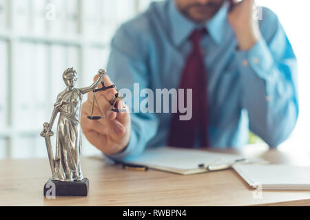 Rechtsanwalt sprechen auf dem mobilen Gerät und spielen mit Gerechtigkeit Maßstab in Law Office, selektiver Fokus auf Statue der Muttergottes Gerechtigkeit Stockfoto