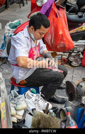 Mann bei der Arbeit als Schuster, Schuhe reparieren, auf dem Bürgersteig in der Altstadt von Hanoi, Vietnam, Asien Stockfoto