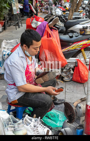 Mann bei der Arbeit als Schuster, Schuhe reparieren, auf dem Bürgersteig in der Altstadt von Hanoi, Vietnam, Asien Stockfoto