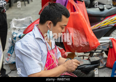 Mann bei der Arbeit als Schuster, Schuhe reparieren, auf dem Bürgersteig in der Altstadt von Hanoi, Vietnam, Asien Stockfoto