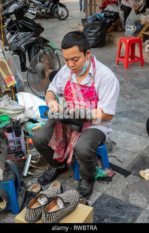 Mann bei der Arbeit als Schuster, Schuhe reparieren, auf dem Bürgersteig in der Altstadt von Hanoi, Vietnam, Asien Stockfoto