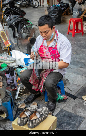 Mann bei der Arbeit als Schuster, Schuhe reparieren, auf dem Bürgersteig in der Altstadt von Hanoi, Vietnam, Asien Stockfoto