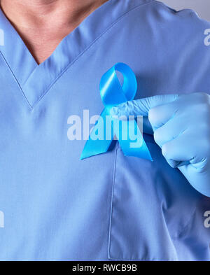 Arzt in der blauen Uniform und Latex Handschuhe mit einem blauen Band in der Hand, ein Symbol für die Bekämpfung und Behandlung von Prostatakrebs Stockfoto