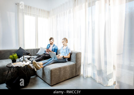 Mann und Frau gekleidet lässig in blauen Shirts mit Laptop und Telefon zu Hause Couch sitzen. In der breiten Ansicht mit Kopie Raum Stockfoto