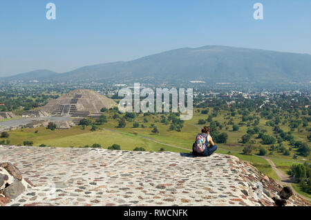 Frau sitzt auf der Spitze der Pyramide der Sonne und die Pyramide des Mondes im Hintergrund in Teotihuacan, Mexiko Stockfoto