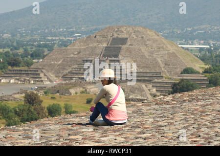 Frau sitzt auf der Spitze der Pyramide der Sonne und die Pyramide des Mondes im Hintergrund in Teotihuacan, Mexiko Stockfoto