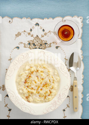 Cremiger Milchreis mit Ahornsirup in dekoriert Schüssel auf Tischset von Overhead. Stockfoto