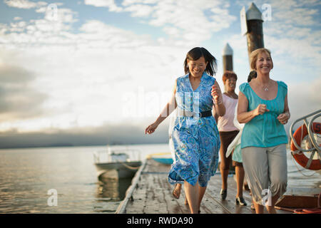 Drei reife weibliche Freunde lachen, wenn sie Spaß an einem hölzernen Pier zusammen haben. Stockfoto