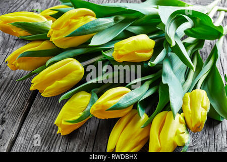 Strauß gelber Farbe frische schöne Tulpen mit Blätter auf einem alten rustikalen Holztisch, Blumenstrauß als Geschenk zum Tag der Frau von gelb Tulpe Blume Stockfoto