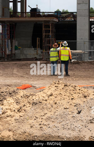 2 Bauarbeiter in hardhats und Warnwesten mit Blick auf die Gebäude, die sie Arbeiten. Stockfoto