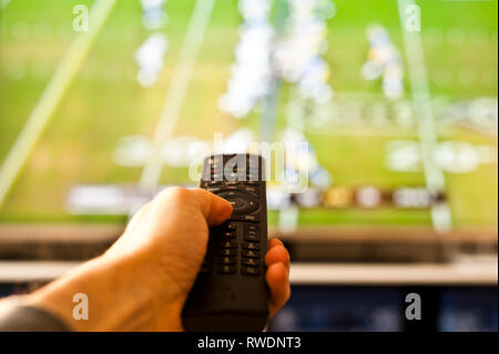 Hand mit einer Fernbedienung vor dem TV-Bildschirm Stockfoto