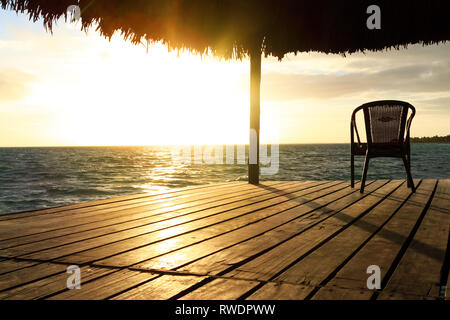 Exotischen Pavillon aus Holz und Stuhl am Strand bei Sonnenuntergang oder Sonnenaufgang. Hintergrund einer Küste mit Sitz, ruhenden Pavillons, Palmen und blaues Wasser in t Stockfoto
