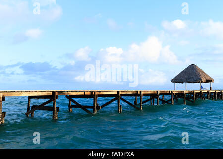 Ribbon Pavillon aus Holz und Stuhl am Strand bei Sonnenuntergang oder Sonnenaufgang. Hintergrund einer Küste mit Sitz, ruhenden Pavillons, Palmen und blaues Wasser in t Stockfoto