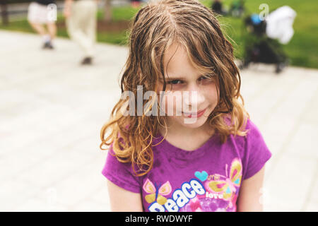 Ein 10-jähriges Mädchen mit lockigem Haar blond nasse Haar unglücklich über Ihr Foto in einem Park in Boston, Massachusetts getroffen sieht. Stockfoto