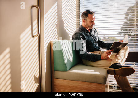 Reife männliche Patienten lesen Sie ein Buch im Wartezimmer des Arztes. Männliche Patienten an der Rezeption der Klinik, auf dem Sofa mit einem Buch sitzen. Stockfoto