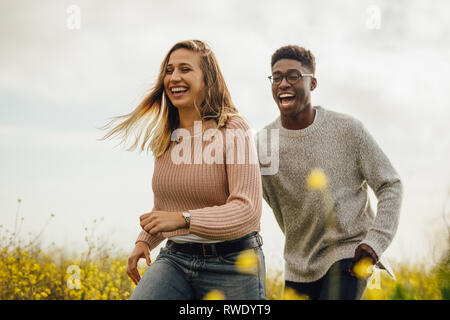 Glücklich der Mann und die Frau, die auf der Wiese Spaß haben. Paar spielen und laufen durch eine blühende Wiese im Freien. Stockfoto