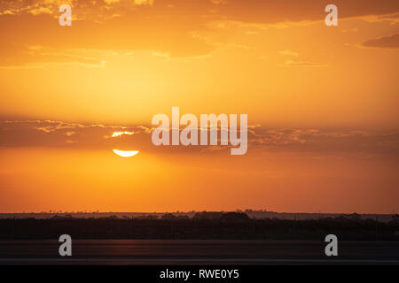 Die Sonne teilweise hinter Cloud in einem orange Sonnenuntergang über Felder in Victoria Australien Stockfoto