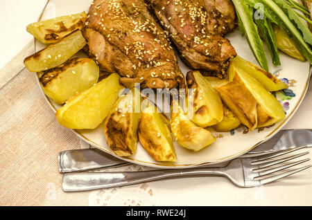 Fayence Platte mit Bratkartoffeln und Huhn, überzogen mit weißer Sesam und schwarzem Pfeffer, neben dem Salat Pfeffer liegen auf einem weissen Papier Serviette. Stockfoto