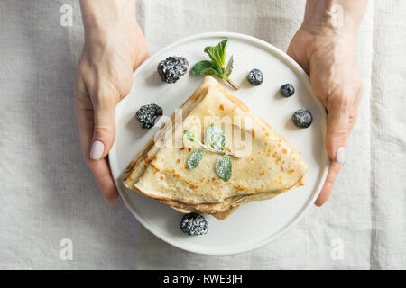 Leckere traditionelle russische Pfannkuchen mit Heidelbeeren. Russische Pfannkuchen in weiblicher Hand. Ansicht von oben. Pfannkuchen Woche. Regionale Lebensmittel. Stockfoto