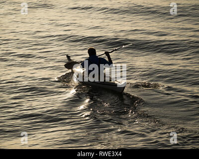 Ein einsamer Mann paddelt ein Kajak bei Sonnenuntergang in Silhouette Auf ruhigem Wasser mit Kopie Raum Wasser Vollformat Stockfoto