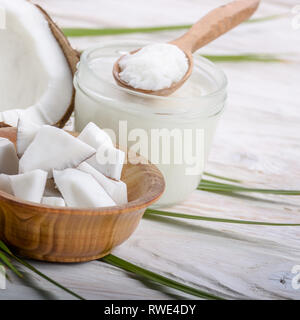 Coconut shell Schwer öl in Glas und Kokosnuss Fleischstücke in Schüssel auf weiße Holztisch Stockfoto