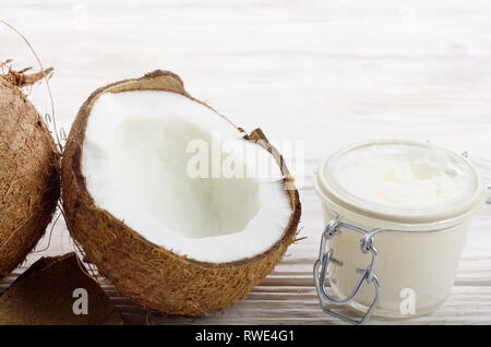 Hintergrund der Kokosnuss, Kokosnussschalen, Schwer öl in luftdichten Glas Glas auf weissem Holztisch Stockfoto