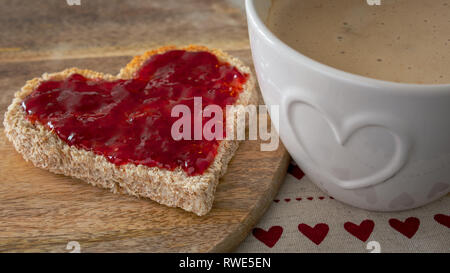 Romantisches Frühstück, herzförmige Toast mit Erdbeermarmelade und Kaffee Stockfoto