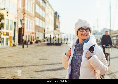 Portrait einer jungen kaukasischen Europäischen Frau Tourist in Gläser für den Blick auf einen weißen Hut und eine Daunenjacke mit einem schwarzen Rucksack auf einer alten E posing Stockfoto