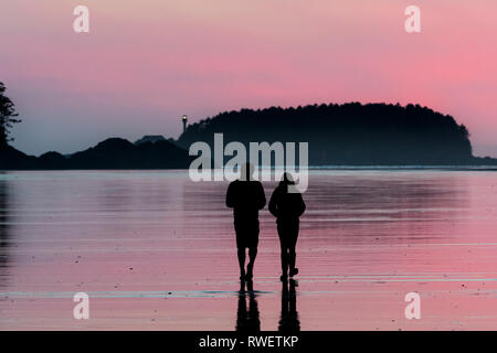 Ein junges Paar Spaziergänge entlang Chesterman Beach in der Nähe von Tofino, British Columbia. Lennard Island Lighthouse ist im Hintergrund. Stockfoto