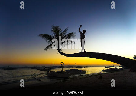 Junge Klettern und Balancieren auf Palmen bei Sonnenuntergang - Panglao - Bohol, Philippinen Stockfoto