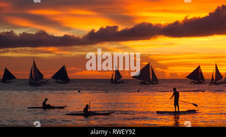 Kajakfahrer, Paddleboarder und Segelboote mit Fiery orange Sonnenuntergang - Boracay Island, Panay - Philippinen Stockfoto