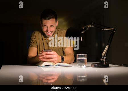Jungen gutaussehenden Mann zu Hause studieren, mit Smartphone, suchen am Telefon lächeln Stockfoto