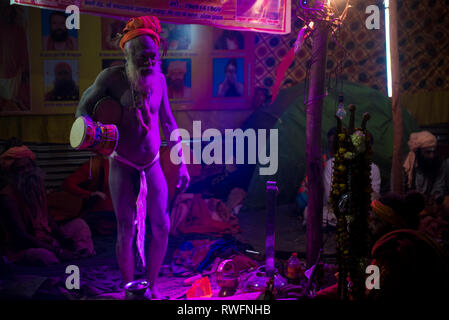 Allahabad/Indien vom 14. Januar 2019 Naga Sadhu indischen Priester Musikinstrument spielen Hand Drum damroo in seinem Zelt am Prayagraj Kumbh Mela in Allahaba Stockfoto