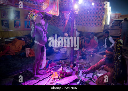 Allahabad/Indien vom 14. Januar 2019 Naga Sadhu indischen Priester Musikinstrument spielen Hand Drum damroo in seinem Zelt am Prayagraj Kumbh Mela in Allahaba Stockfoto