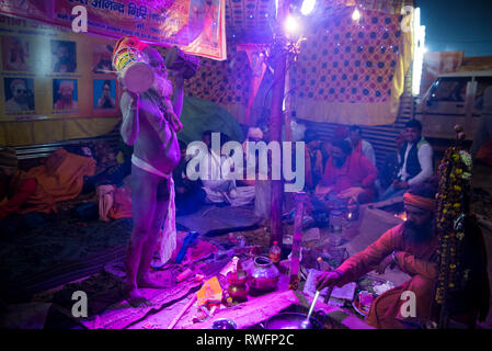 Allahabad/Indien vom 14. Januar 2019 Naga Sadhu indischen Priester Musikinstrument spielen Hand Drum damroo in seinem Zelt am Prayagraj Kumbh Mela in Allahaba Stockfoto