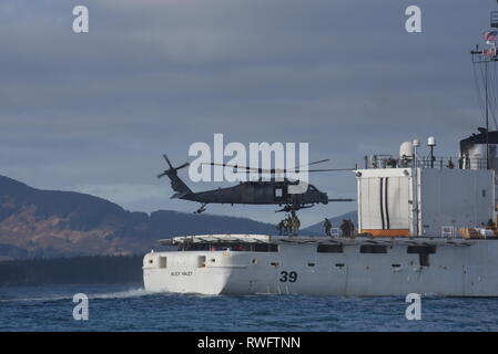 Mehrere Mitglieder der Küstenwache Maritime Security Response Team West eine Leiter in eine 176 Flügel, Rettung, 210Th Squadron Alaska Air National Guard HH-60 Pavehawk Hubschrauber aus dem Flight Deck der Coast Guard Cutter Alex Haley (WMEC 39) in einer gemeinsamen Übung in Chiniak Bay, Alaska, Feb 23, 2019. Die Teammitglieder sind geschult und technisch fortgeschrittene Techniken beherrschen, bundesstaatlicher und lokaler Partner, die Nation von Bedrohungen sowohl auf See und in der Luft zu schützen. U.S. Coast Guard Foto von Petty Officer 3. Klasse Lauren Dean. Stockfoto