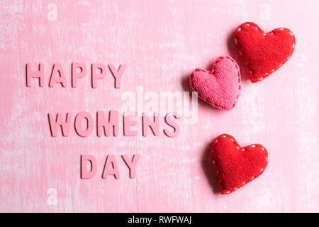 Tag der Frauen Konzept. Rote Herzen mit Holz Buchstaben bilden Wort Happy Tag der Frauen auf rosa und weißen Holzmöbeln Hintergrund geschrieben. Stockfoto