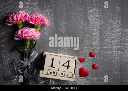 Valentines Tag und liebe Konzept. Rosa Nelke Blume mit Februar 14 Texte auf hölzernen Block Kalender und roten Herzen und auf grauen Holz- Hintergrund. Stockfoto