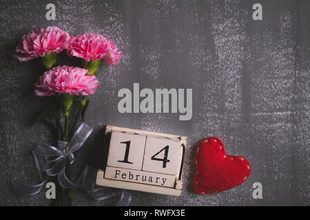Valentines Tag und liebe Konzept. Rosa Nelke Blume mit Februar 14 Texte auf hölzernen Block Kalender und roten Herzen und auf grauen Holz- Hintergrund. Stockfoto