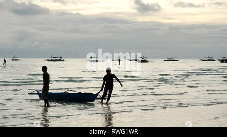 Kleine Fischerboote am Strand von zwei Männern - Silhouetten auf Boracay Island, Panay - Philippinen gezogen Stockfoto