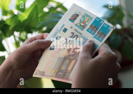 In Frauenhand einen Umschlag mit Briefmarken von Hong Kong und Euro-banknoten Stockfoto